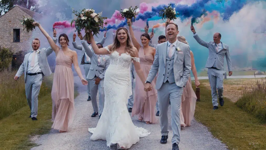 Bride and groom surrounded by wedding party with vibrant smoke effects.