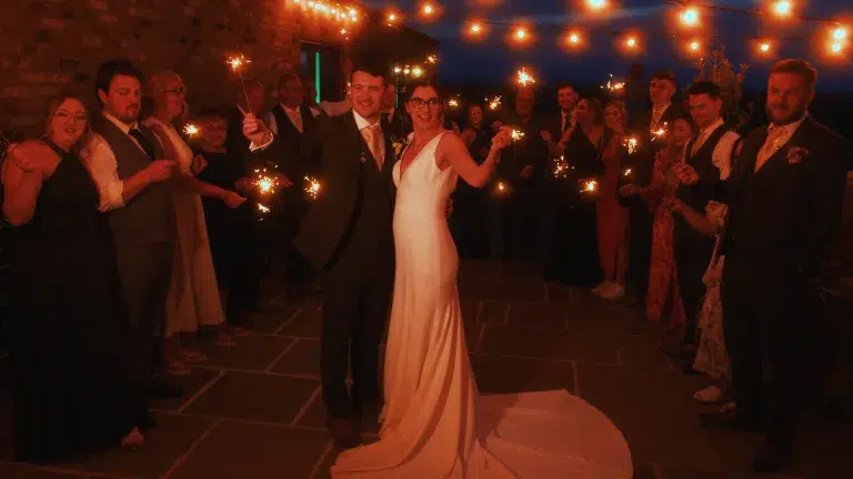 Couple surrounded by guests and sparklers, mid-celebration